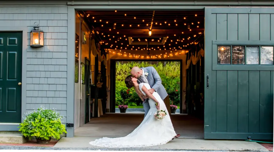 Couple kiss in the barn doorway under string lights